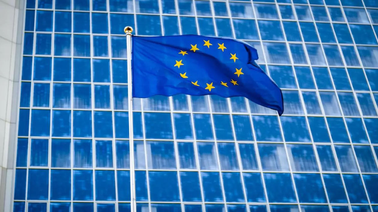Imagine creativă cu steagul Uniunii Europene arborat în fața unei clădiri administrative din Bruxelles cu geamuri de culoare albastră