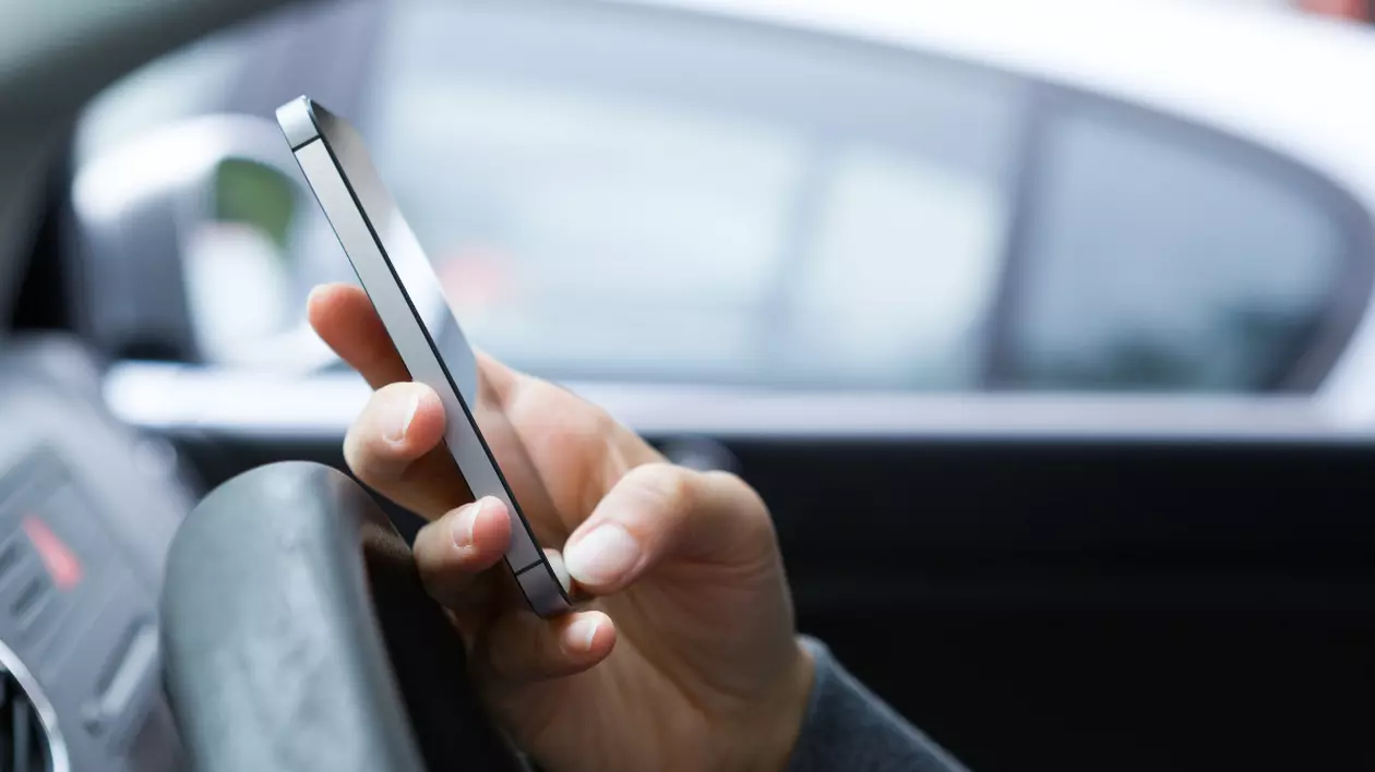 Un bărbat care ține un telefon în mână, la volan