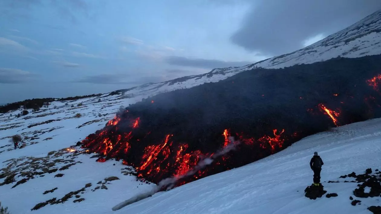 Un turist se uită la lava care curge de pe Muntele Etna în timpul unei erupții a vulcanului pe 14 februarie 2025