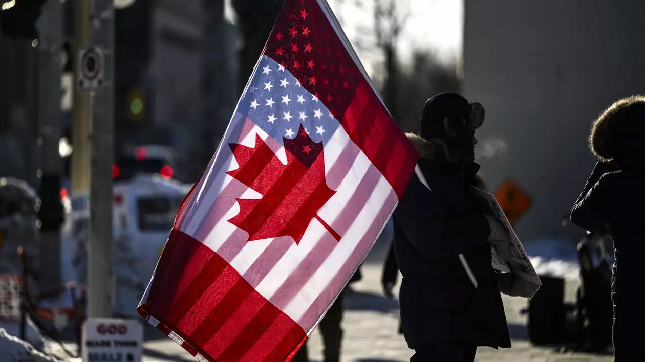 Un protestatar canadian, cu steagurile suprapuse ale SUA și Canadei, în fața Parlamentului de la Ottawa, pe 1 februarie 2025 Foto: Profimedia