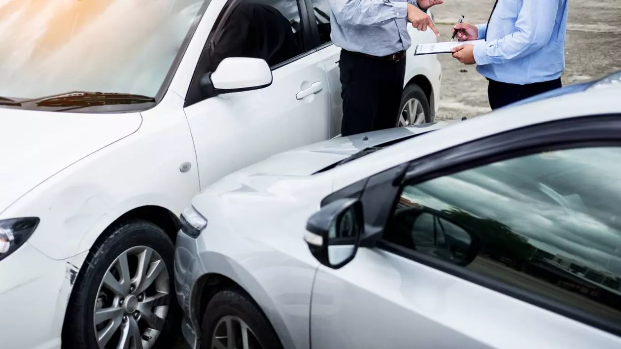 accident auto între două mașini, una albă și una argintie. doi bărbați îmbrăcați în cămăși și pantaloni discută și completează documente, probabil un formular de constatare amiabilă. Unul dintre ei pare să indice cu mâna un anumit detaliu, posibil legat de accident.