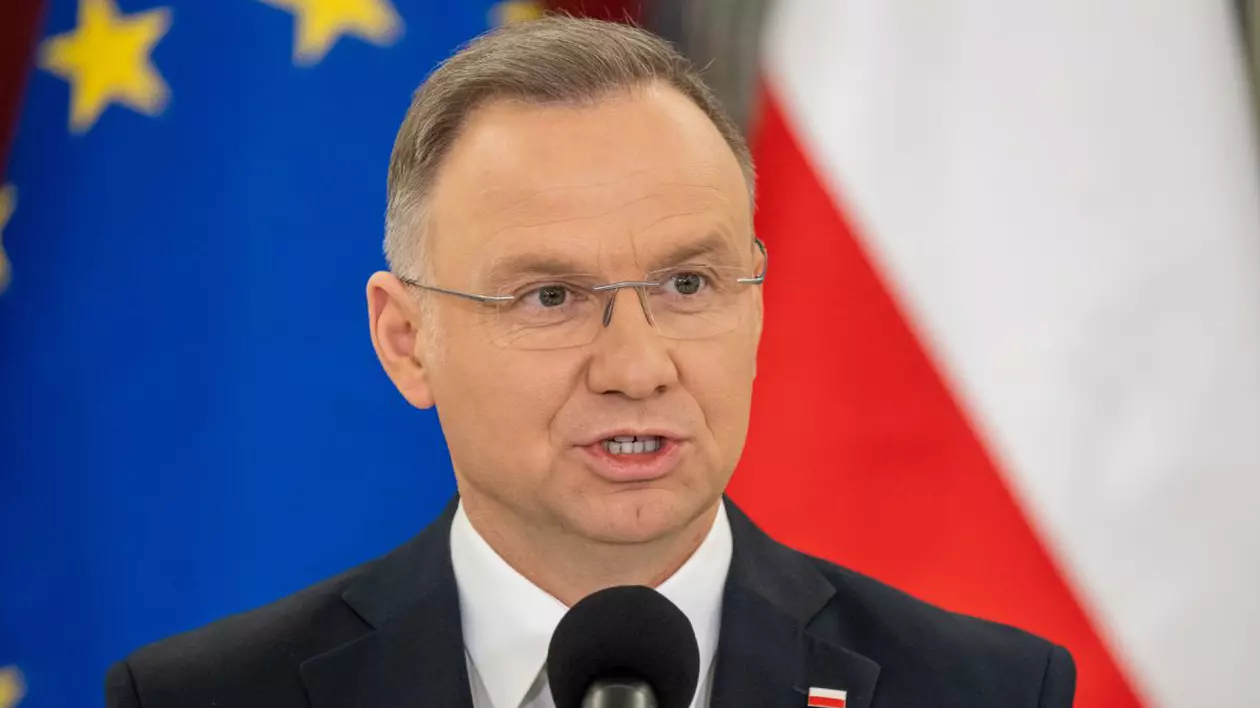Andrzej Duda, președintele Poloniei, în prim-plan, îmbrăcat în costum cu cămașă albă, cu steagurile Poloniei și Uniunii Europene pe fundal