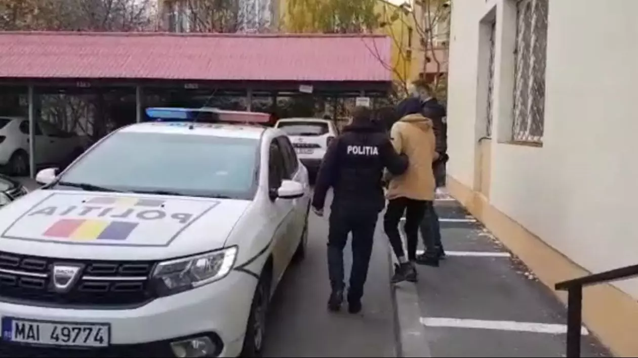 Bărbatul din Craiova (cu spatele), acuzat că i-a amenințat pe oamenii legii cu un excavator, a fost prins și este ținut de brațe de polițiști, iar lângă ei se află o mașină a Poliției