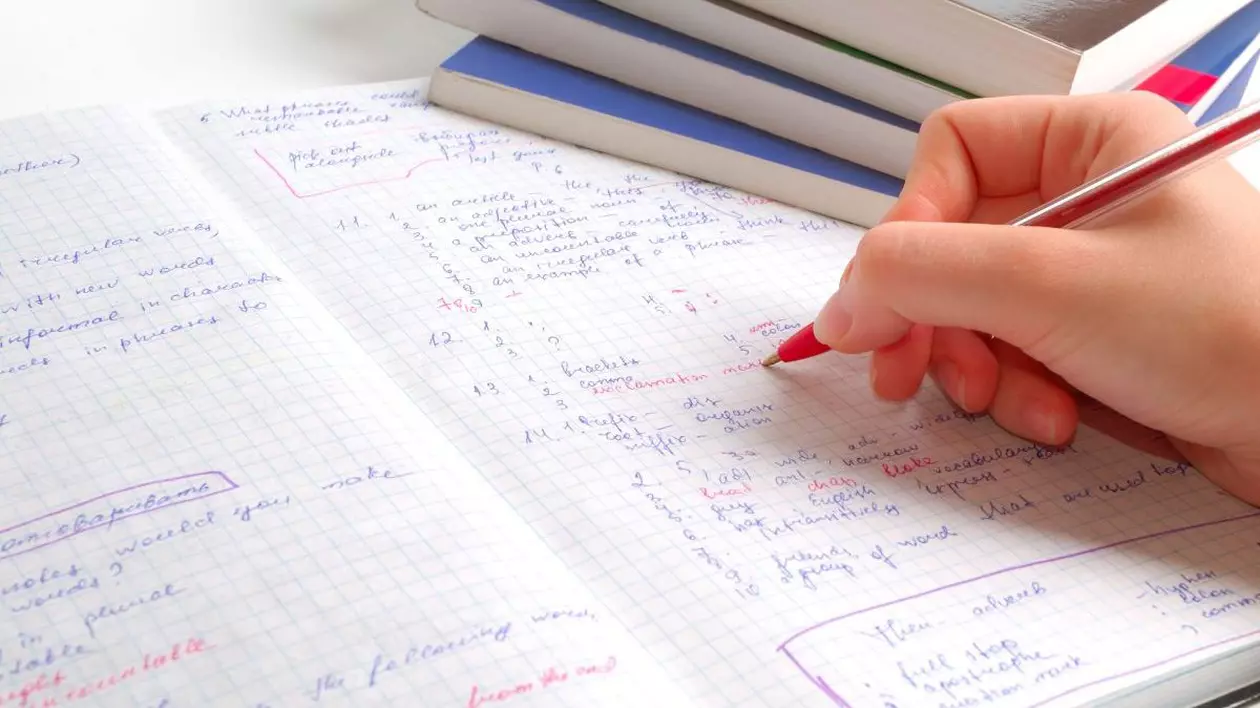 Un profesor corectează cu pixul roșu tema unui elev făcută pe un caiet