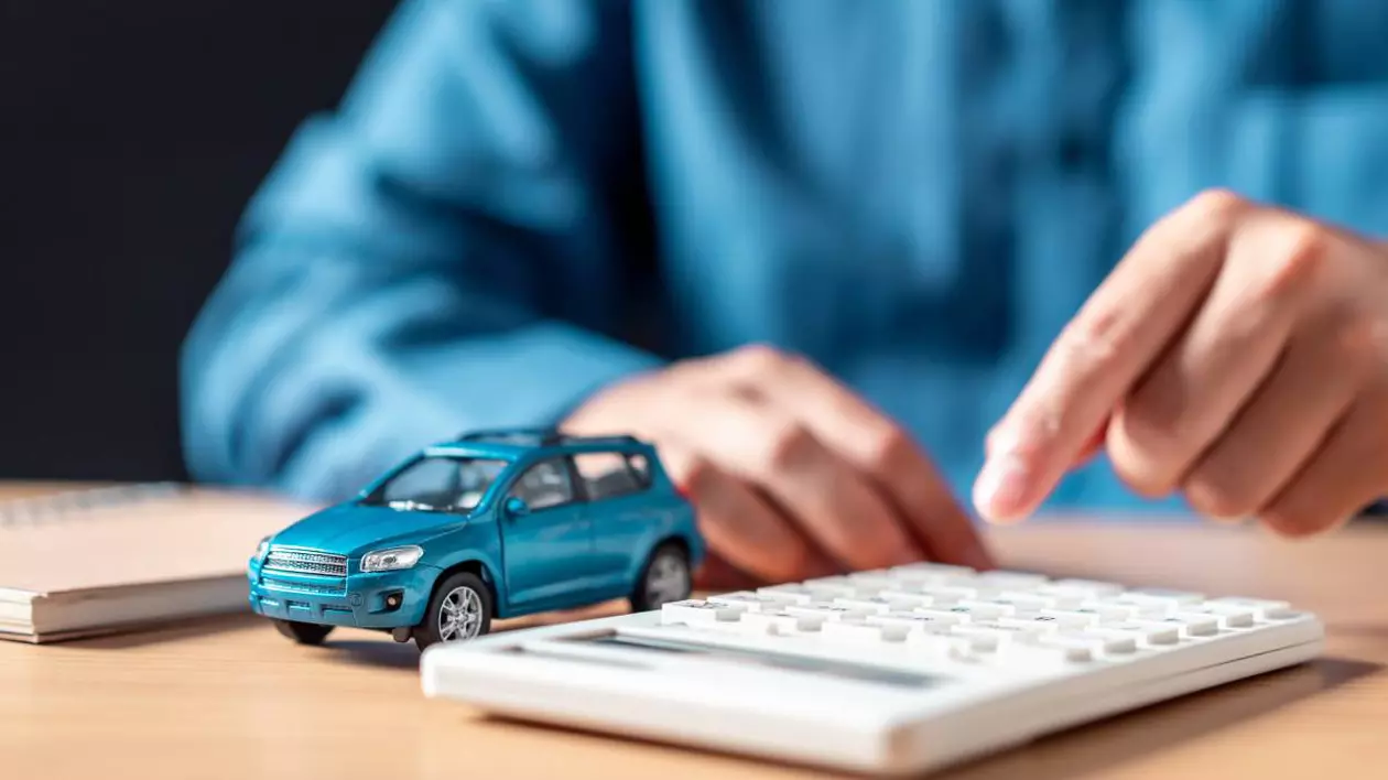 mana unui barbat care tasteaza pe un calculator, langa este o masina in miniatura albastra