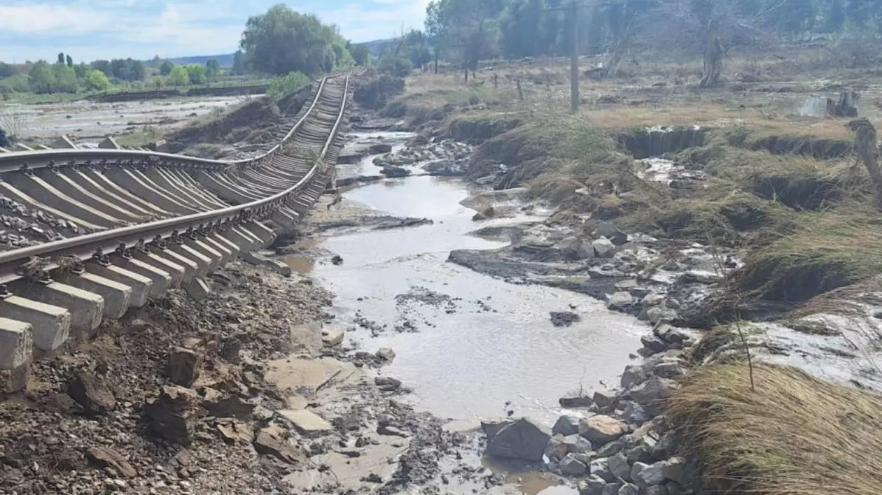 fotografie cu o cale ferata distrusa in urma unor inundatii. langa este un drum pietruit inundat de apa