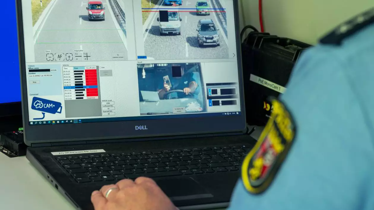 un ofițer de poliție, purtând uniformă albastră cu un ecuson pe braț, monitorizează activitatea rutieră pe un computer care afișează imagini capturate de pe camere de trafic