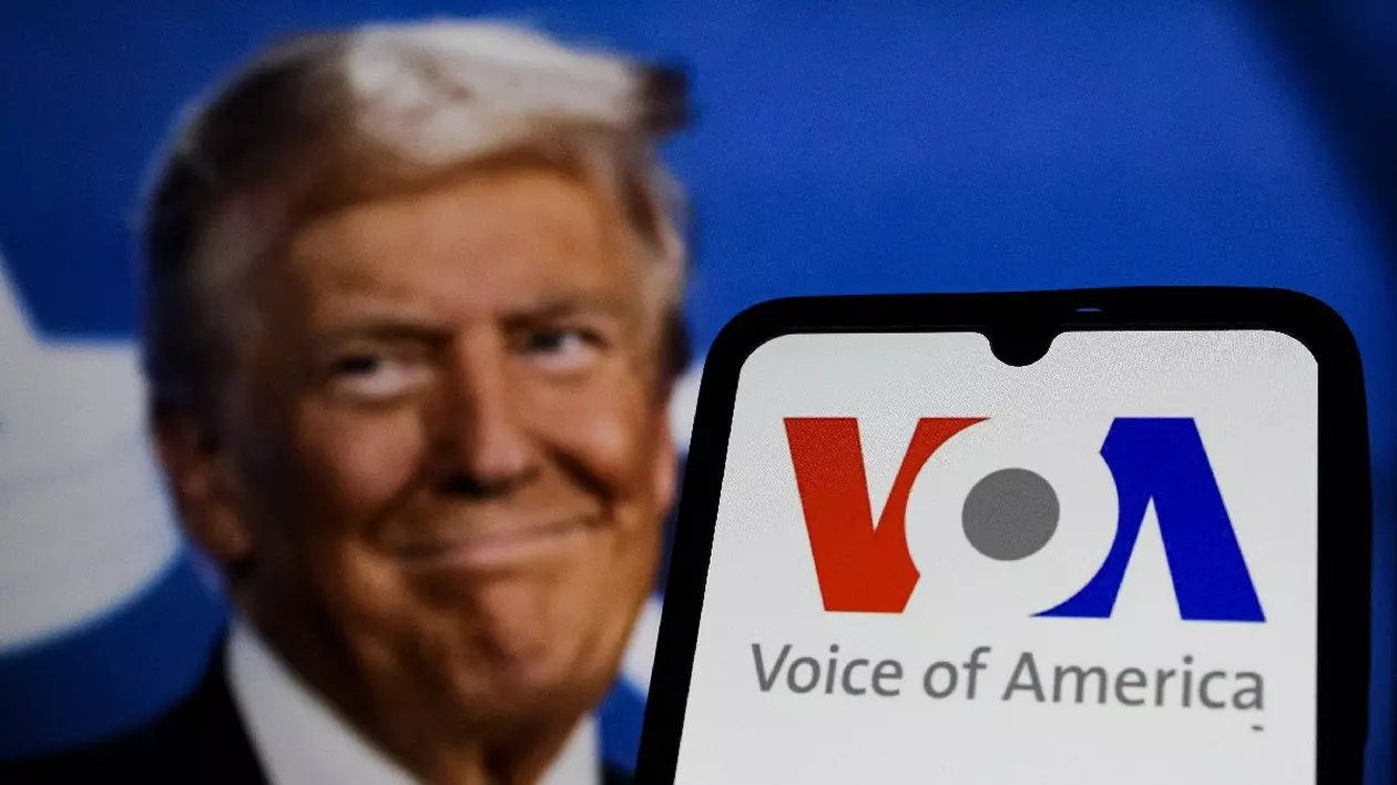n această ilustrație foto, logo-ul Vocii Americii (VOA) apare pe un telefon mobil cu fotografia de profil a președintelui Statelor Unite ale Americii DONALD TRUMP vizibilă în fundal.