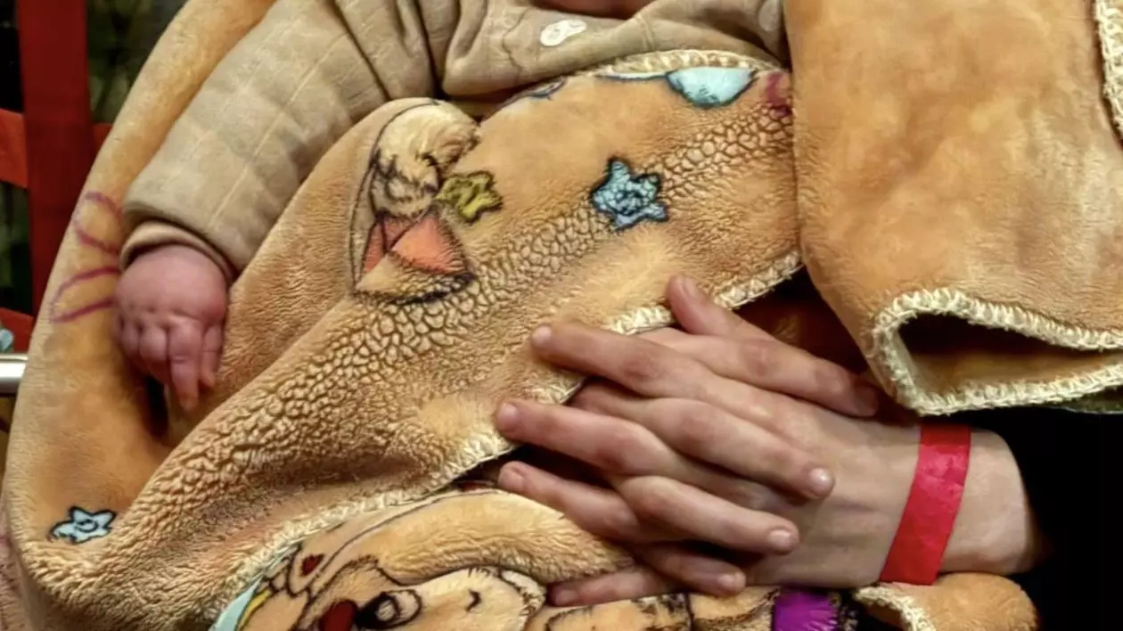 Un copil din Fâșia Gaza, căruia nu i se vede capul, este ținut într-o pătură de mama sa și a fost adus în România pentru tratament, 19 martie 2025