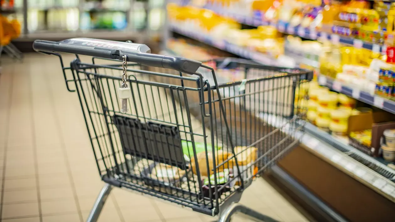Coș de cumpărături cu câteva produse în el, într-un raion al unui supermarket