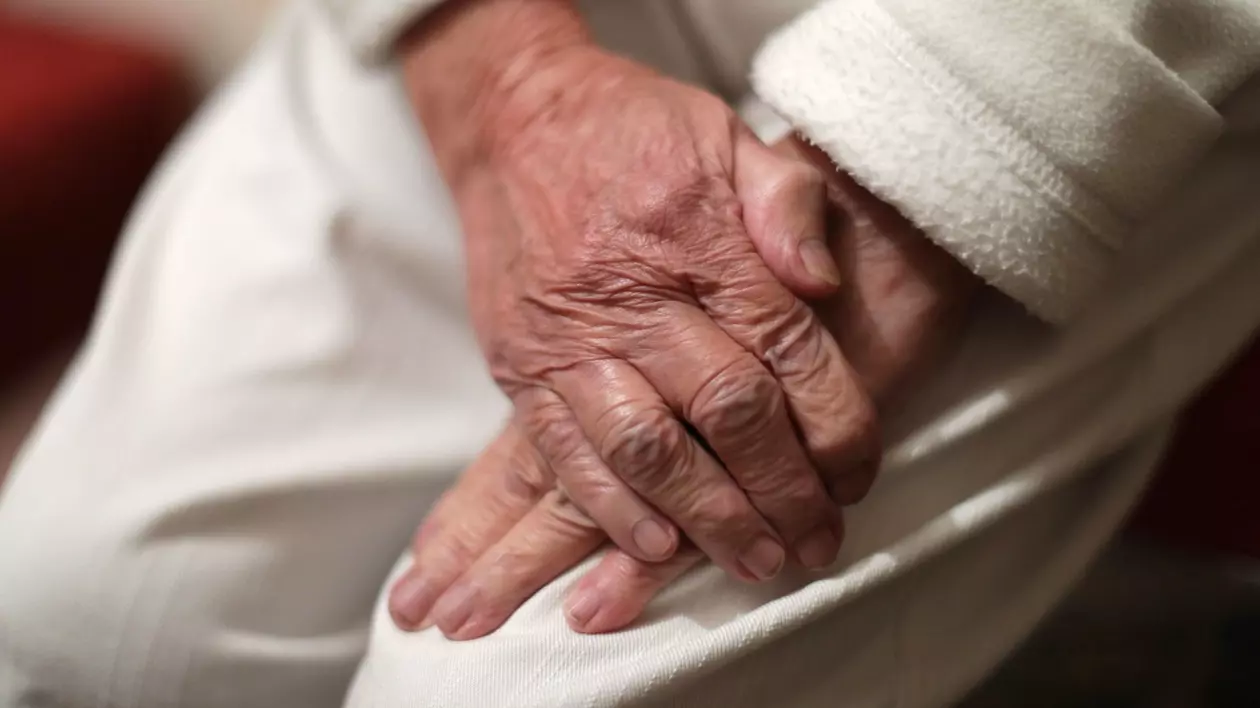 Mâinile unei paciente cu Parkinson, așezate pe picior