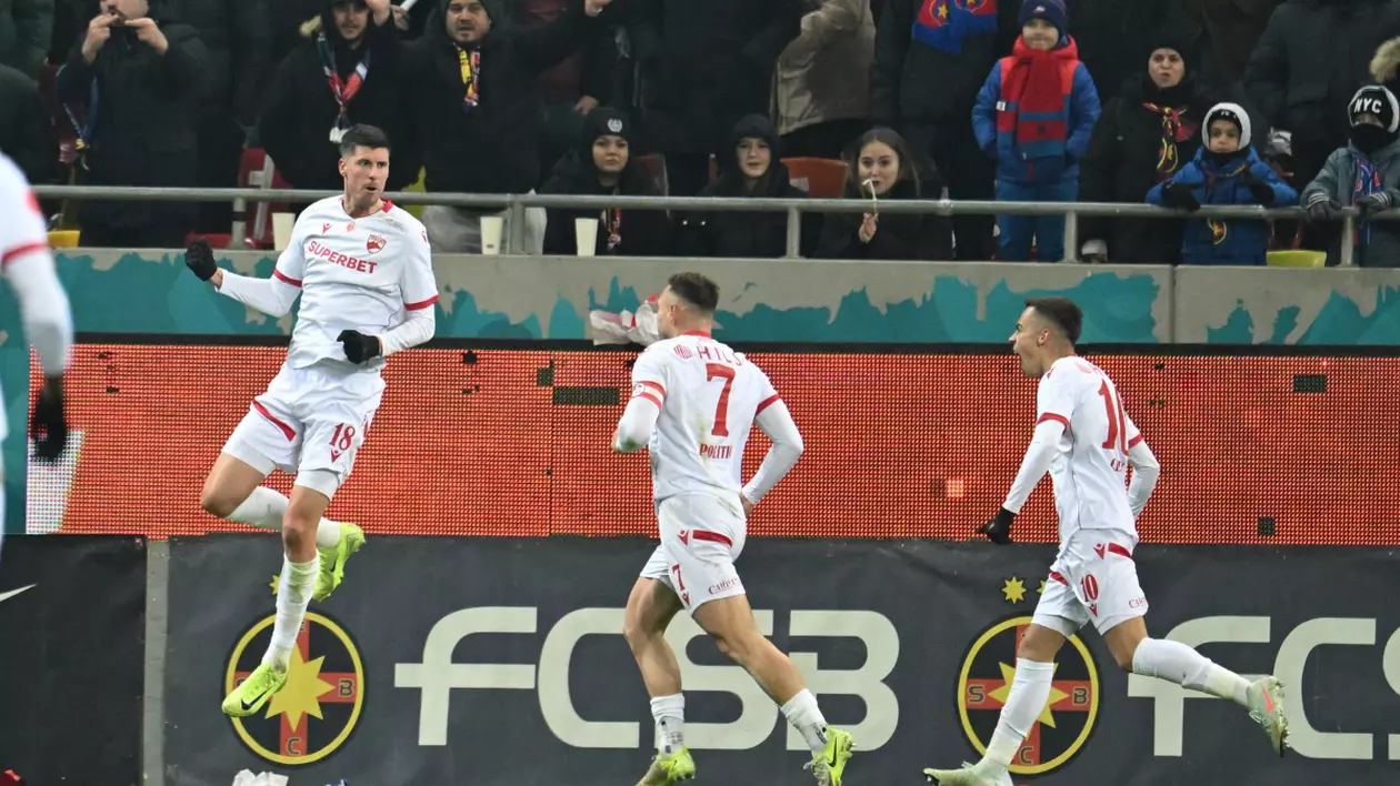 Jucatori de fotbal pe teren, in timpul meciului. În spate se pot vedea suporterii din tribună.