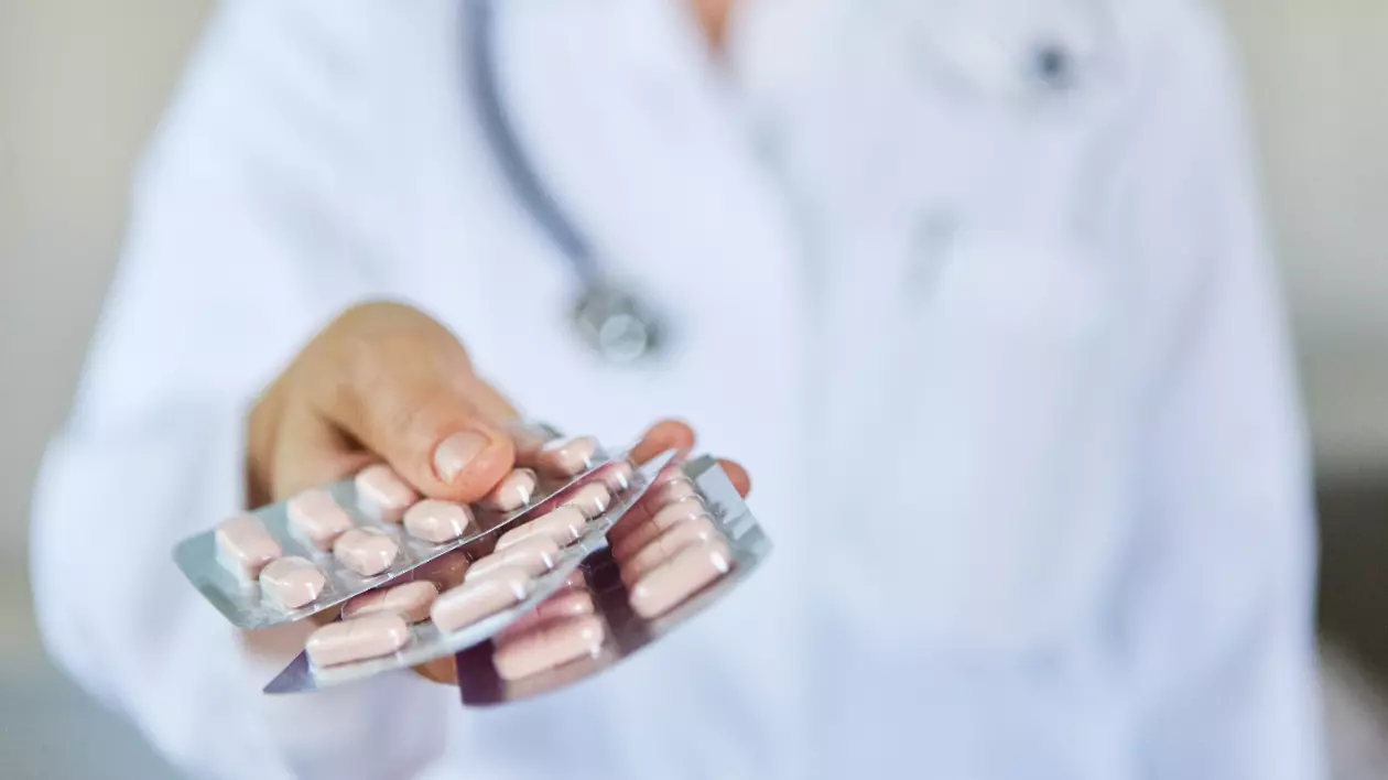 Un doctor cu stetoscop și halat alb, care ține în mână medicamente