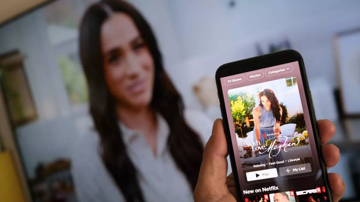 telefon mobil deschis pe aplicatia netflix, pe fundal un ecran mare pe care ruleaza filmul Ducesei de Sussex, Meghan Markle