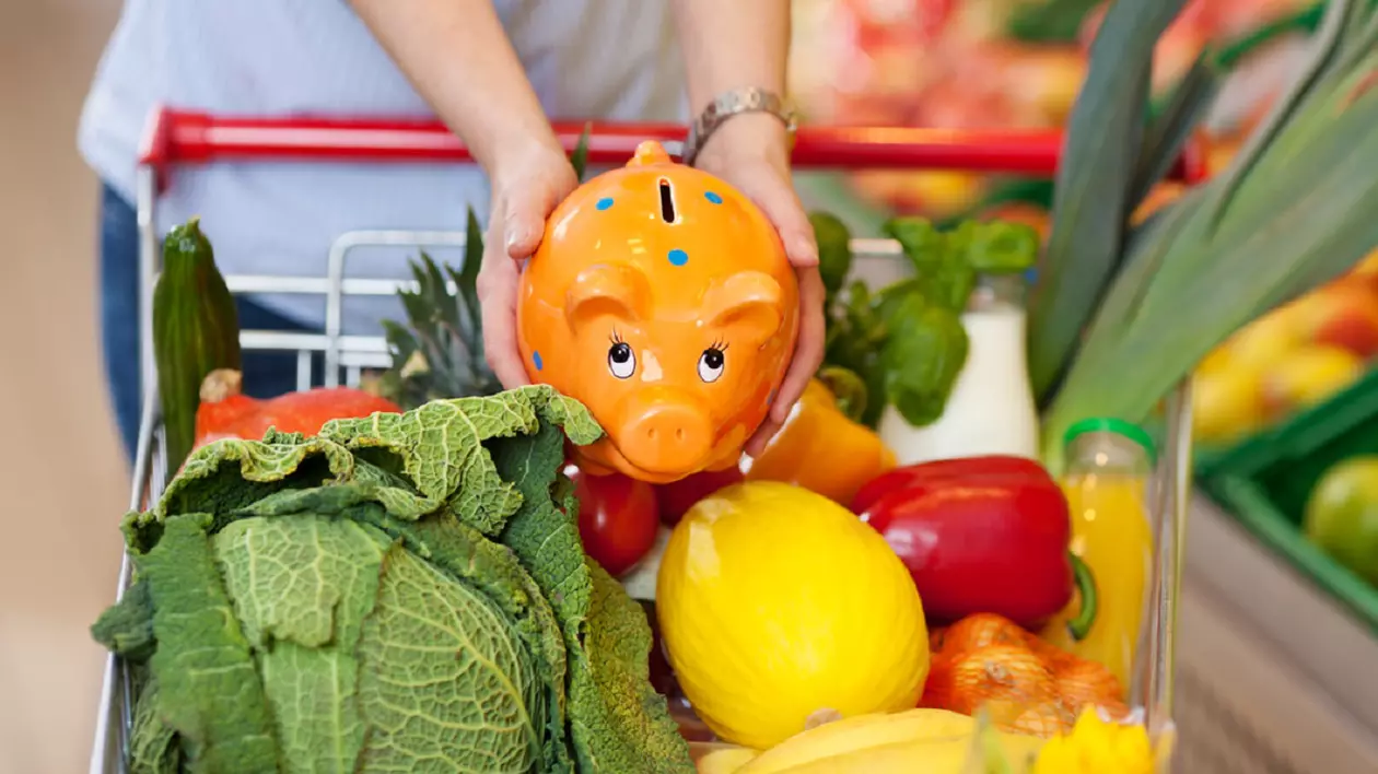 Ce este metoda „6 la 1” prin care poți să faci economie la cumpărături - Imagine cu o femeie care ţine cu ambele mâini o puşculiţă "porcuşor" ceramică, desupra unui cărucior de cumpărături la supermarket