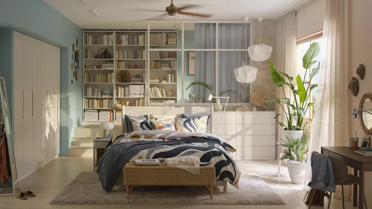 IKEA - poza cu un dormitor luminos, in culorile bej si bleu, avand un pat situat in centru si rafturi in spatele lui.