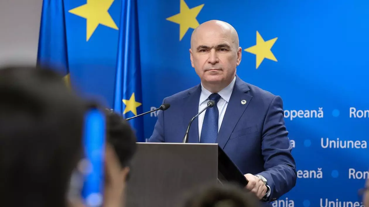 Președintele interimar Ilie Bolojan, îmbrăcat la costum, vorbește cu presa de la pupitru și are în spate steagul UE, cu stele galbene, 6 martie 2025