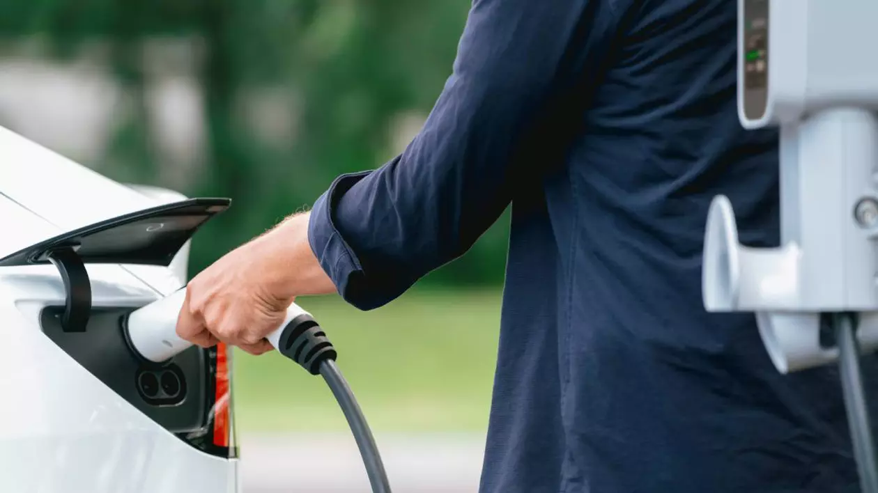 barbat imbracat cu o camasa albastra in timp ce pune la incarcat o masina electrica alba