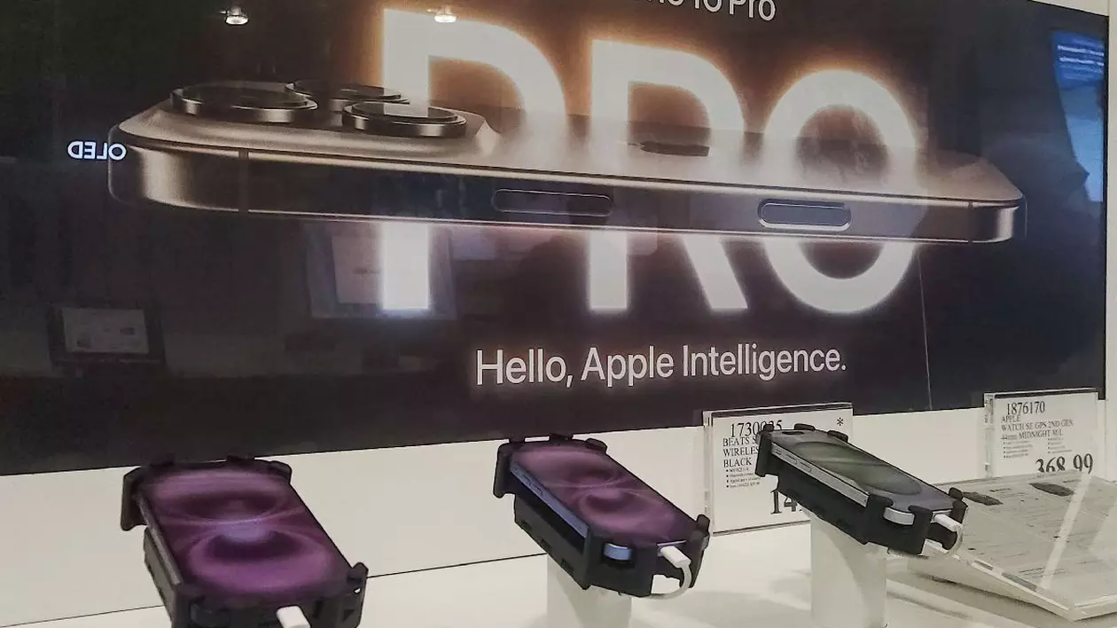 Modele iPhone 16 Pro, expuse într-un magazin Apple, cu o reclamă în fundal.