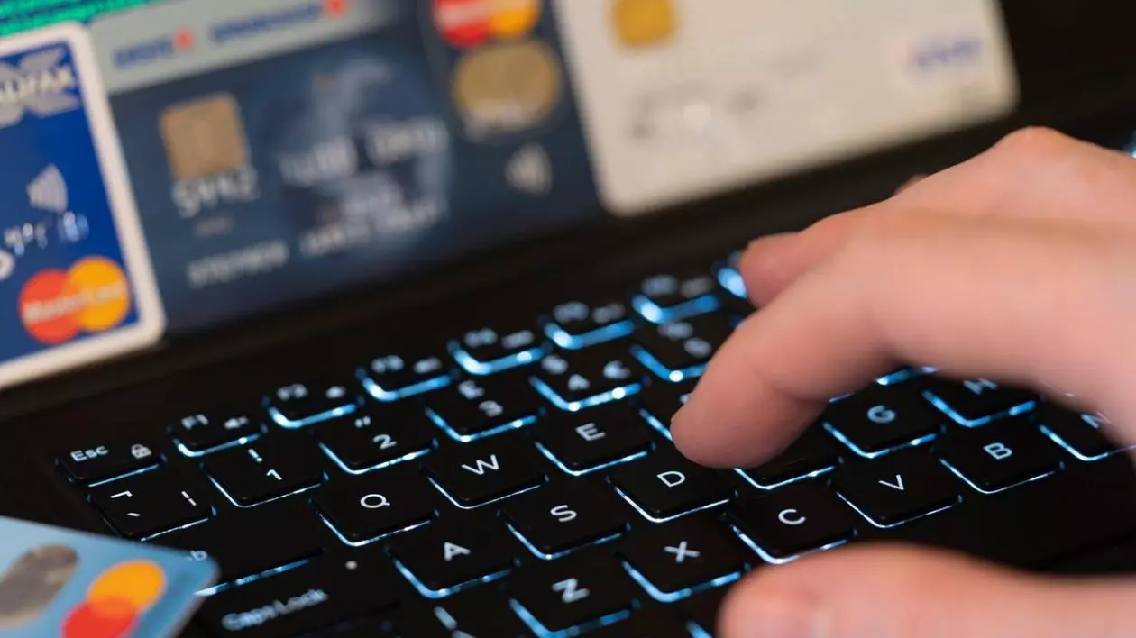 O mână care tastează pe o tastatură cu un ecran de computer și cărți de credit în fundal. Concept: fraudă folosind carduri de credit furate pentru a efectua plăți online Foto: Profimedia Images
