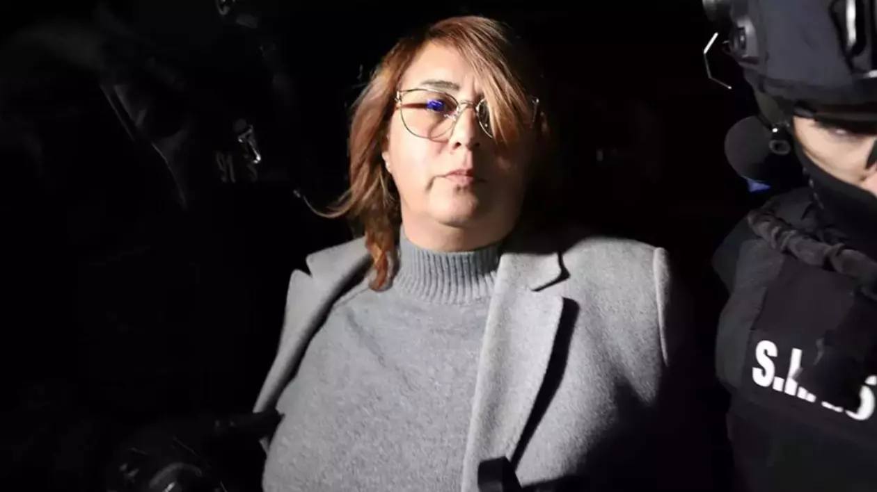 În imagine este Laura Crișan, îmbrăcată cu o bluză și un palton gri