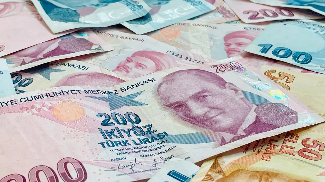 Bancnote lira turceasca de diferite valori așezate pe o suprafață. Culorile predominante sunt nuanțe de roz, albastru și bej