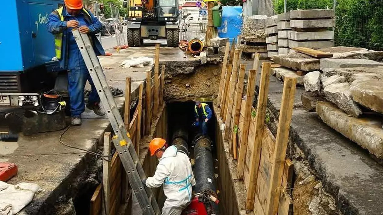 Trei muncitori schimbă conductele de apă într-o zonă din București unde au făcut un șantier, iar unul dintre ei este pe o scară