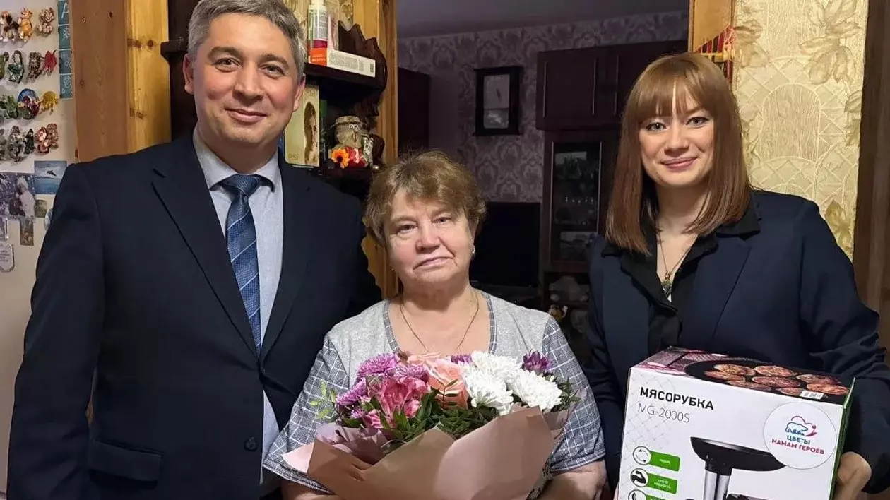 Un bărbat și două femei. O femeie ține în mână un buchet de flori, iar cealaltă o mașină de tocat.