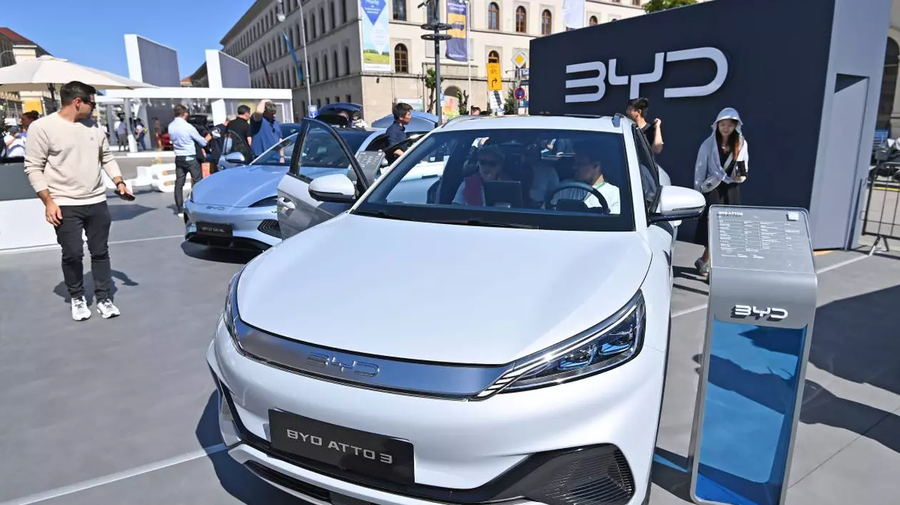 masina electrica alba la o expozitie, prezentare toate detaliile de motorizare, in spate sunt cateva persoane