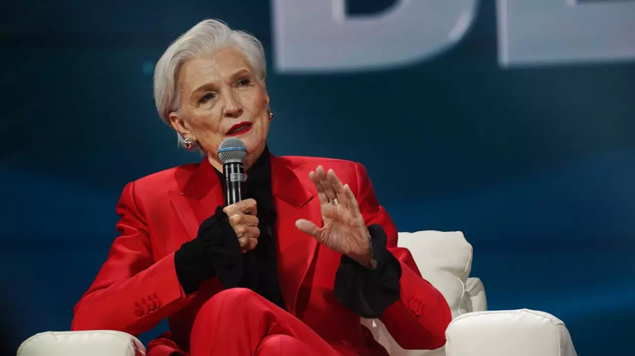 Maye Musk, mama lui Elon Musk, la o conferința de presă, îmbrăcată într-un costum roșu din două piese, cu o cămașă neagră