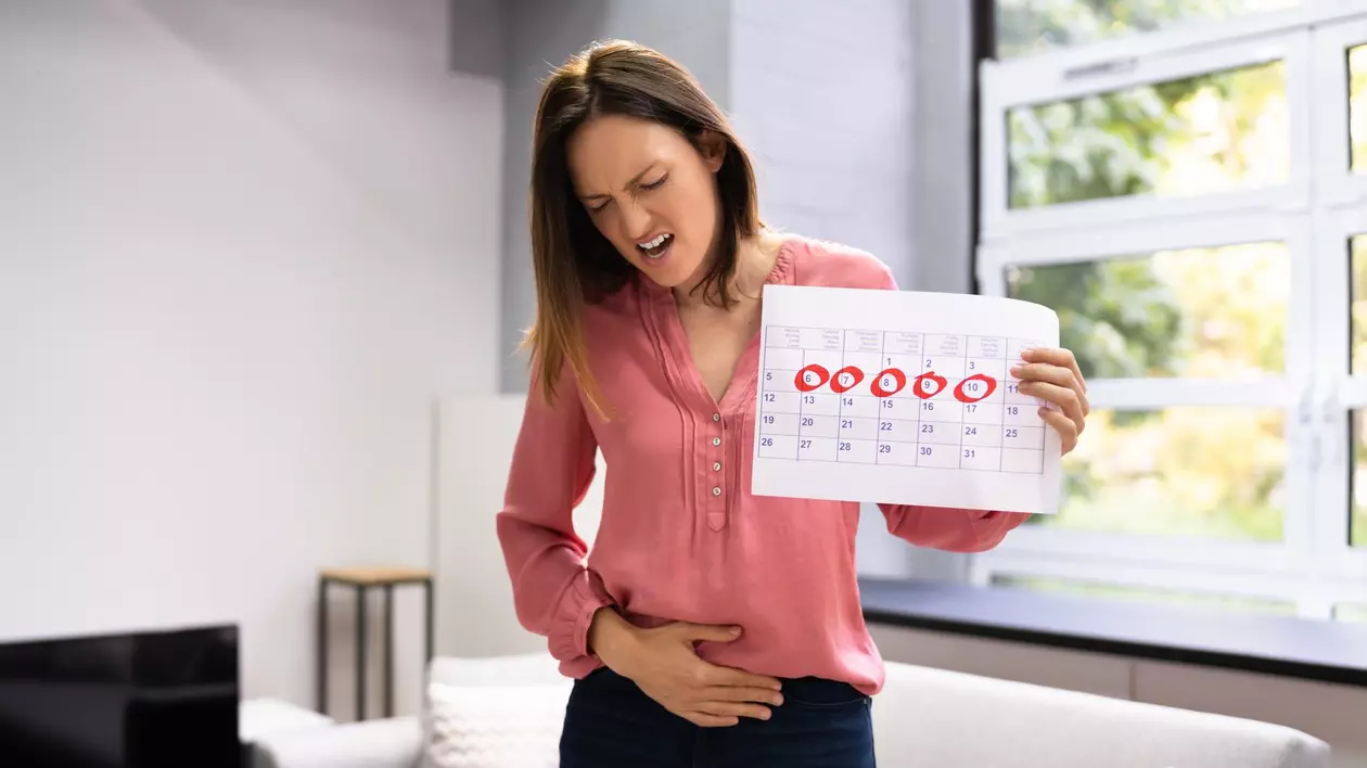Femeie care ține în mână un calendar, iar cu cealaltă își atinge burta