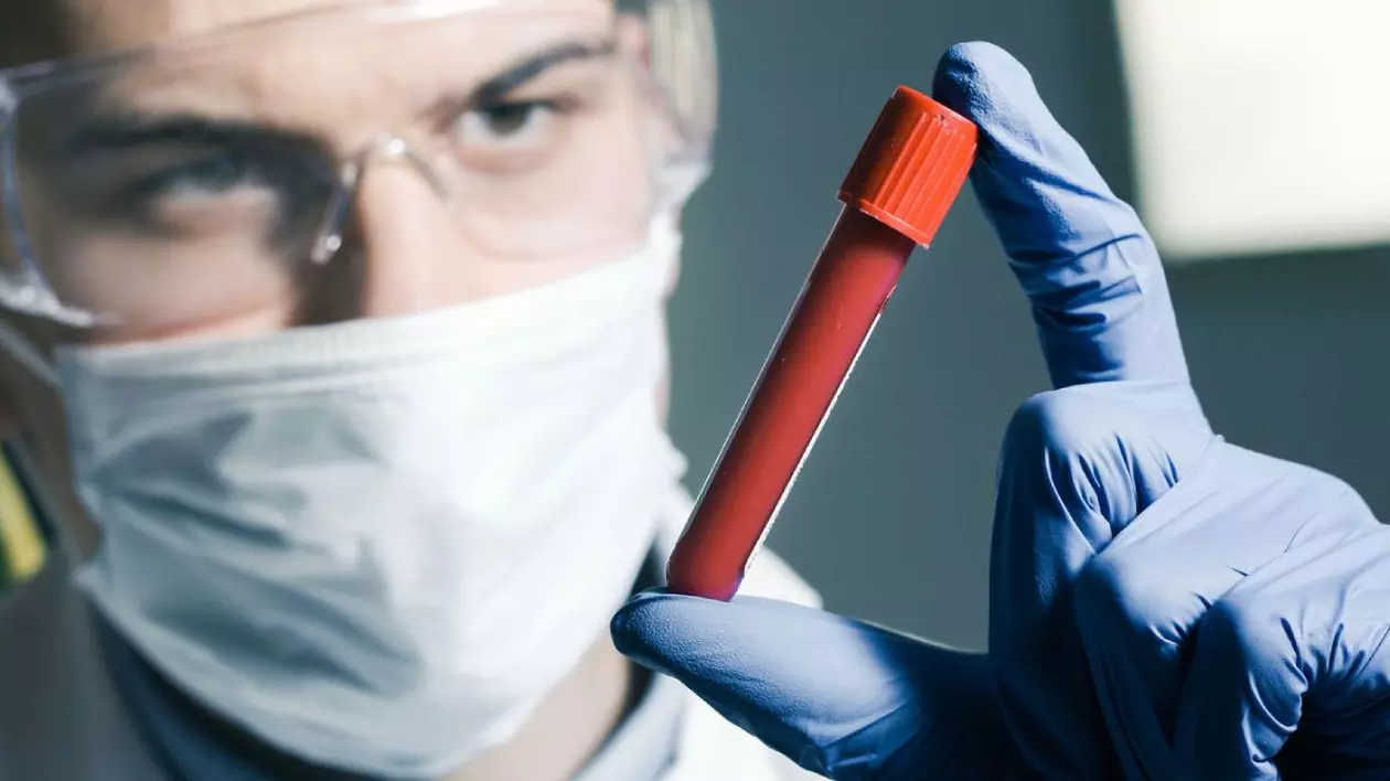 Doctor care ține un tub de probă de sânge pentru testare în mănuși de protecție într-un laborator.