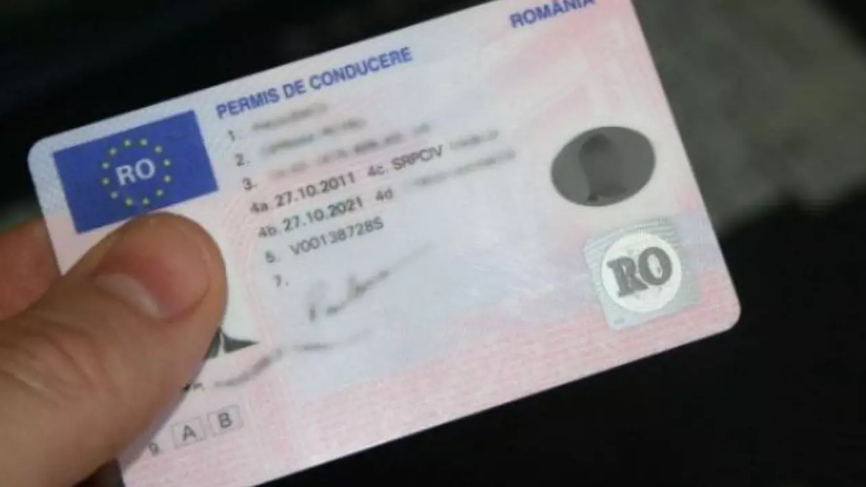 Permis de conducere din România, în prim plan, ținut cu două degete de un bărbat