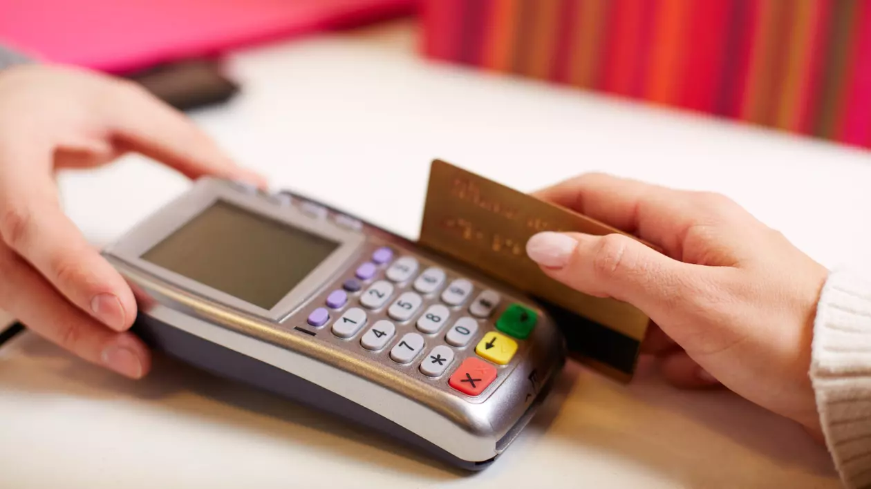 Un aparat POS ținut de o mână de bărbat și o mână de femeie care ține un card de credit