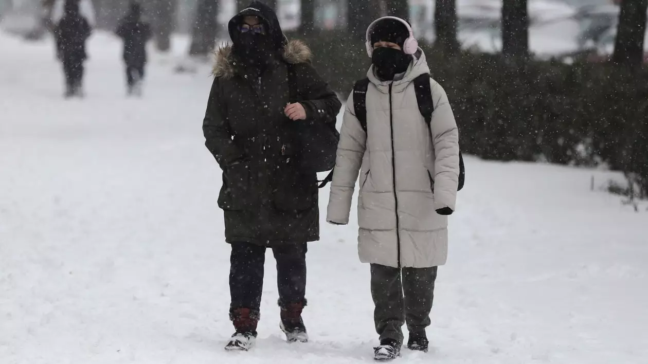 Două femei îmbrăcate cu geci groase de iarnă, cu fulare și căciuli, merg prin zăpadă, în București