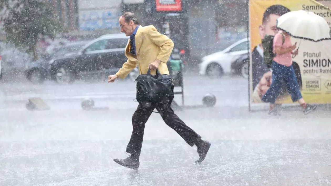 Un bărbat îmbrăcat la sacou galben fuge printr-o ploaie abundentă, iar femeie merge în direcția opusă, având o umbrelă în mână, în București