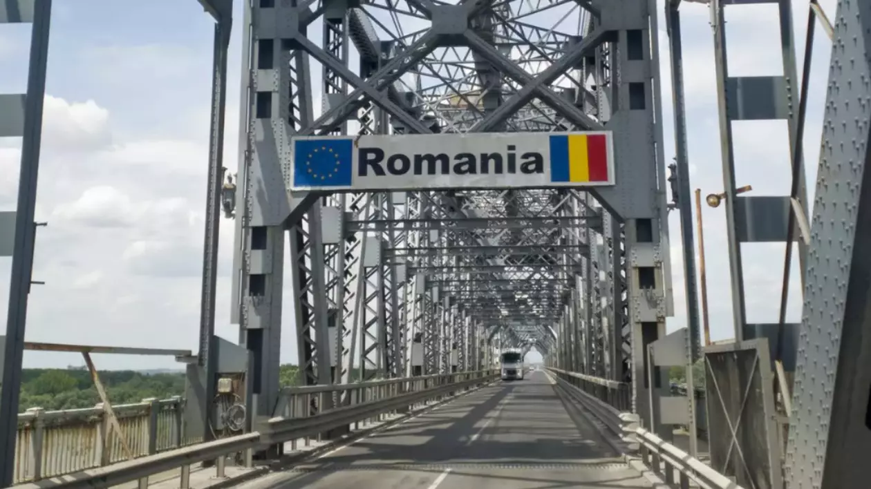 Pod metalic cu o structură de oțel, pe care se află un semn cu inscripția „Romania” alături de steagul Uniunii Europene și steagul României