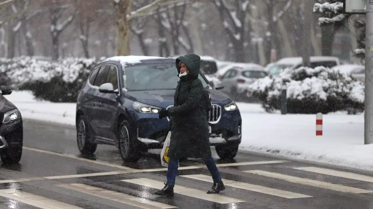 O femeie îmbrăcată cu geacă și glugă traversează strada pe trecerea de pietoni, în timp ce alte mașini au oprit, iar în jur se vede zăpadă. Foto: Libertatea/Dumitru Angelescu