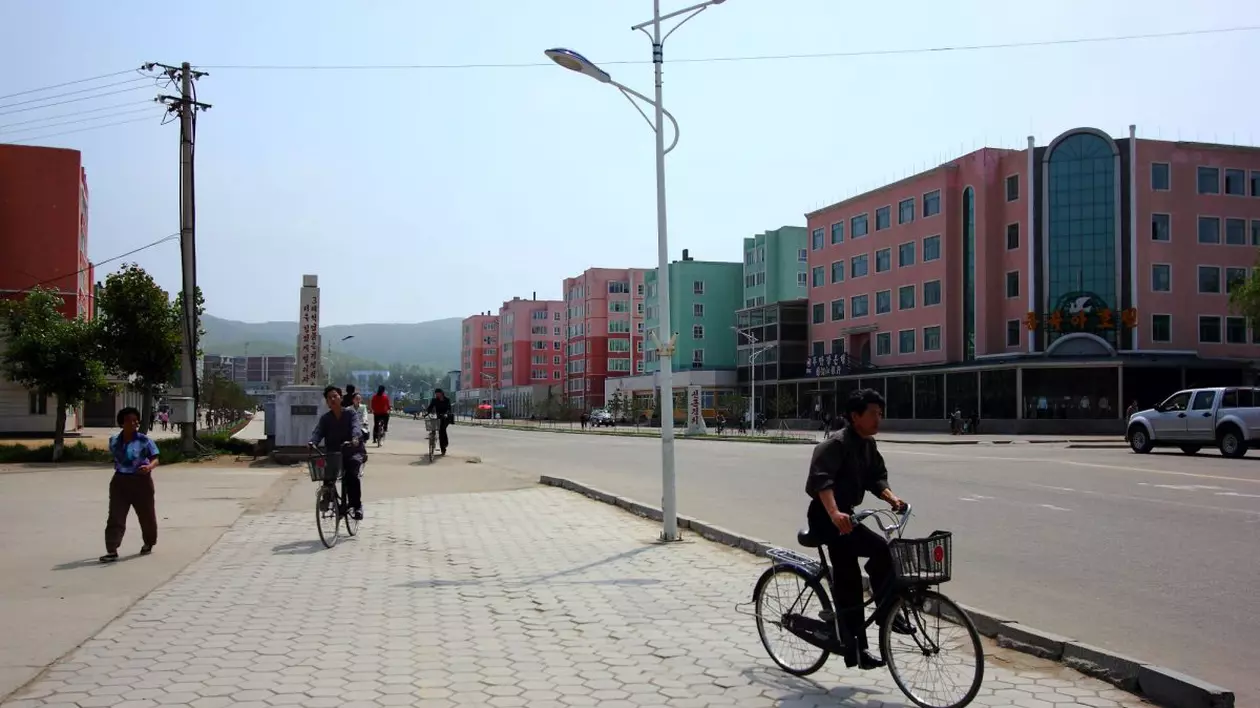 peisaj din rason, coreea de nord, un baiat merge pe bicicleta in partea dreapta, cladirile orasului pe fundal