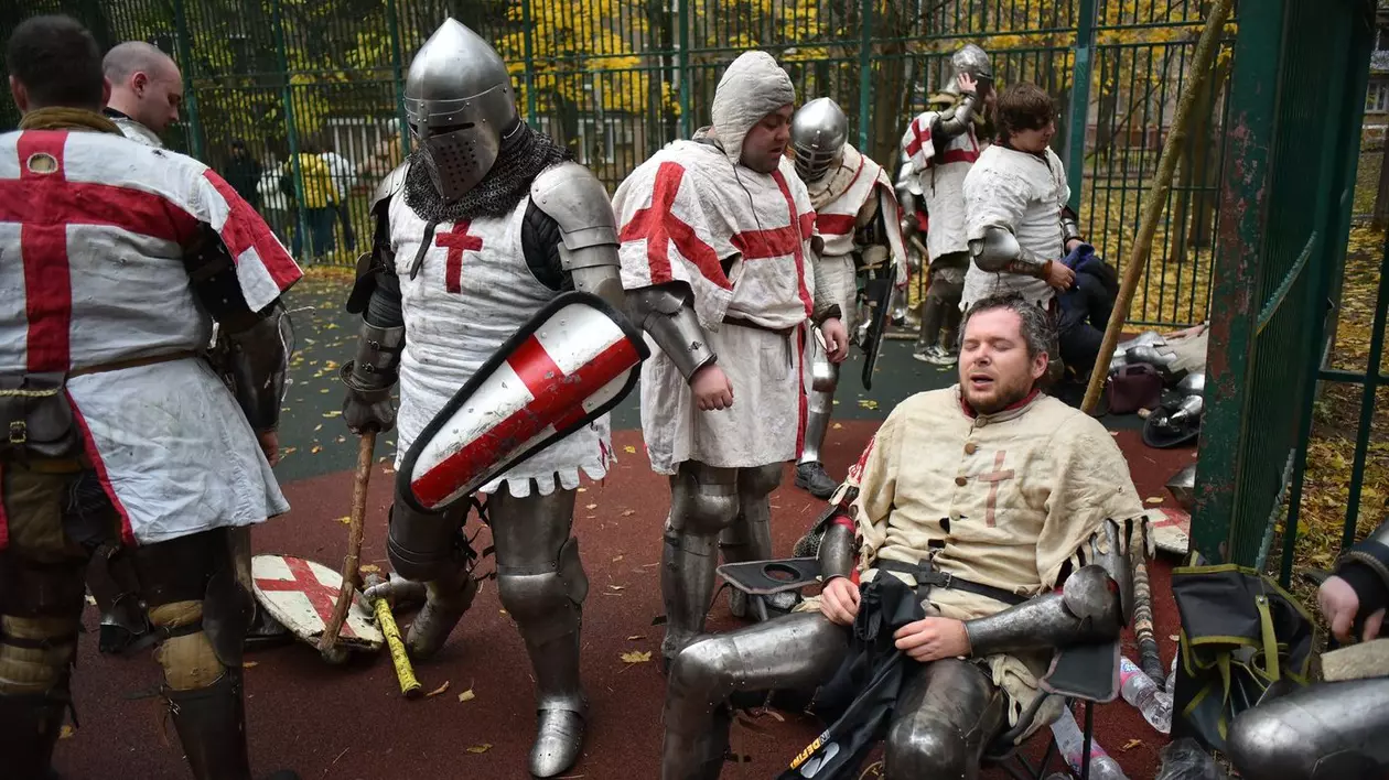 Oameni purtând componente de armură medievală iau parte la un eveniment de luptă amicală desfășurat pe un teren de baschet pentru a menține luptele de stradă medievale vii