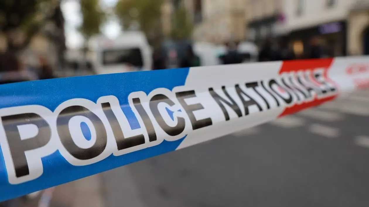 O zonă de pe stradă unde a avut loc o crimă a fost delimitată de poliție și nu se mai trece, iar pe un fundal neclar se vede o mașină de poliție