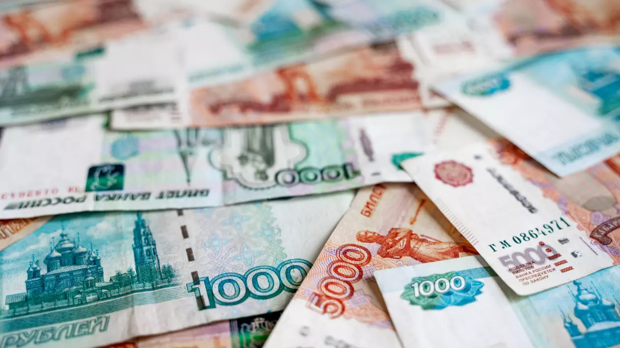 Bancnote de ruble rusesti, de culoare portocaliu, albastru și verde, de diferite valori, împrăștiate pe o suprafață