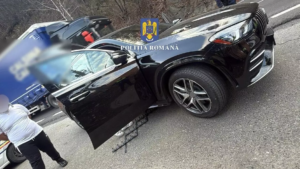 O mașină Mercedes, de culoare neagră, un bărbat supraponderal, îmbrăcat cu un tricou alb și pantaloni negri, încătușat