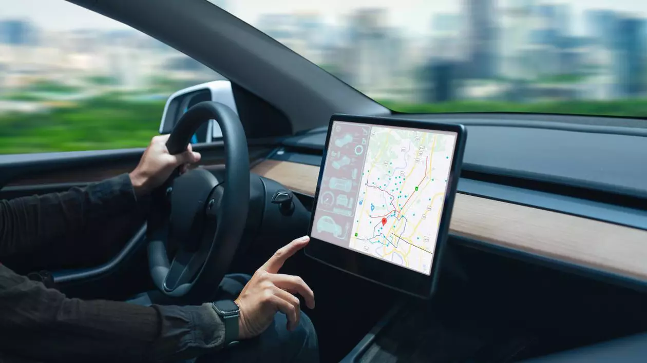 sofer intr-o masina electrica moderna in timp ce seteaza datele de navigare in consola digitala a masinii. in prim plan este prezentat bordul masinii si se observa volanul si un ecran mare pentru navigatie