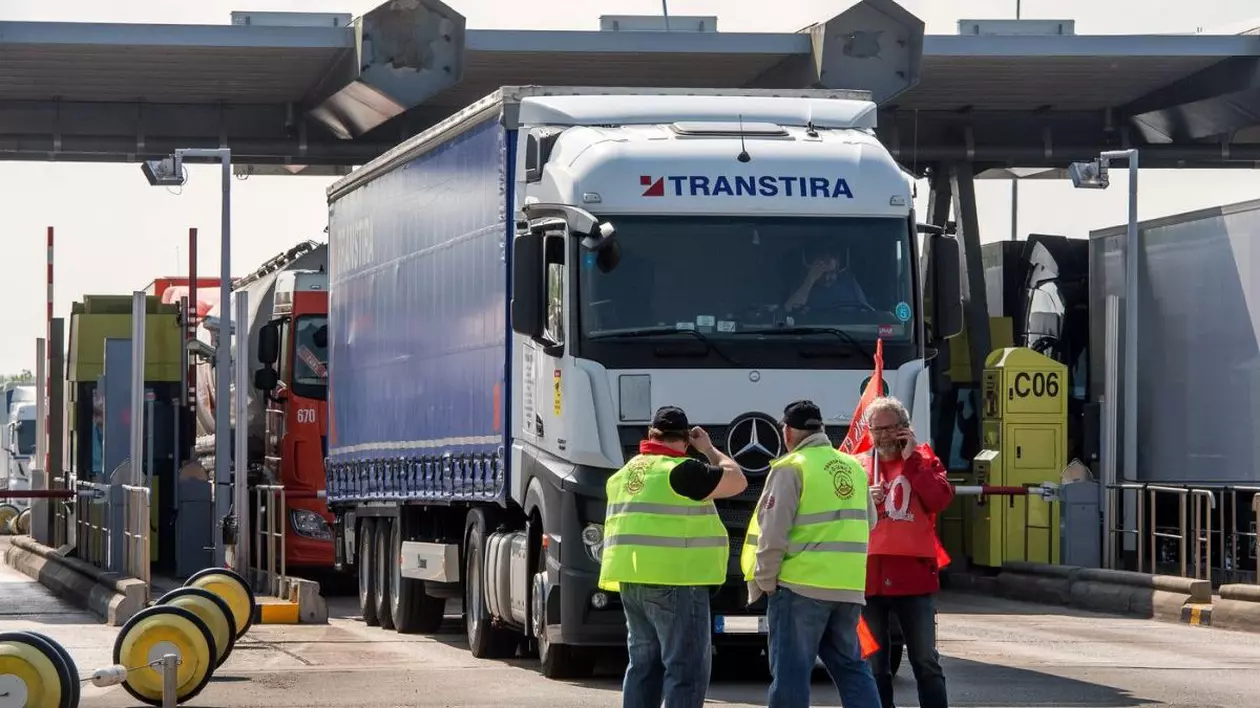 Un TIR, al cărui șofer este în cabină la volan, așteaptă la un punct de taxare în Franța, iar în spatele lui sunt alte mașini