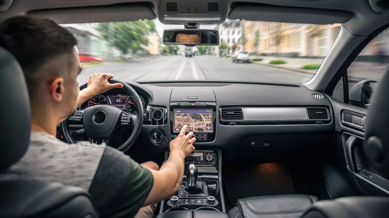 Un bărbat care este la volanul mașinii atinge ecranul unui sistem de navigație GPS