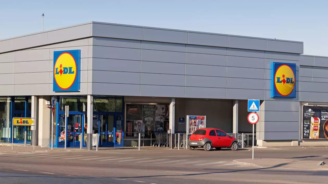 supermarket lidl, in fata magazinului este parcata o masina rosie mica, fotografia cuprinde o parte din parcarea supermarketului