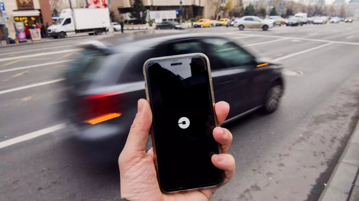 Bărbat care ține un smartphone cu aplicația Uber deschisă și așteaptă o mașină, în București.
