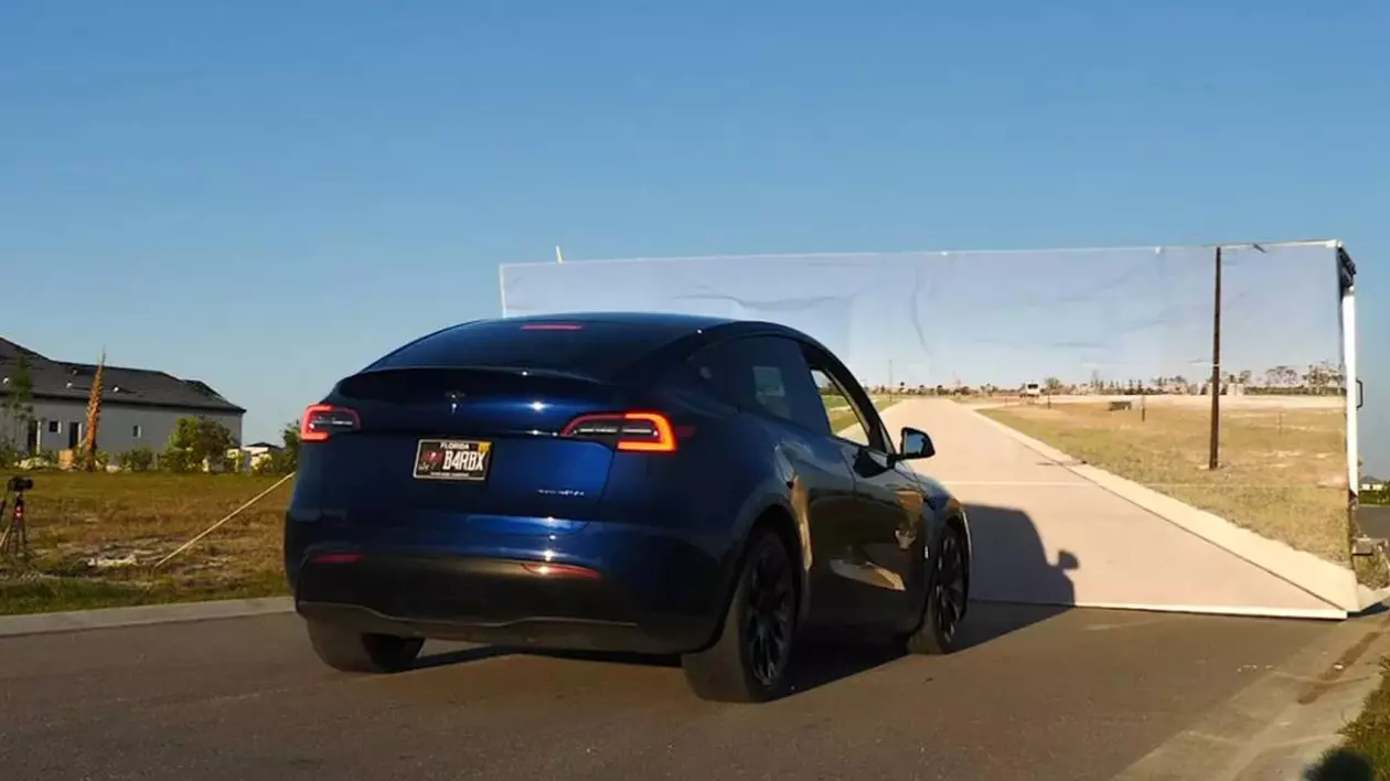 masina tesla model y de culoare albastra in timpul unui test, in fata unui panou care imta peisajul din exterior