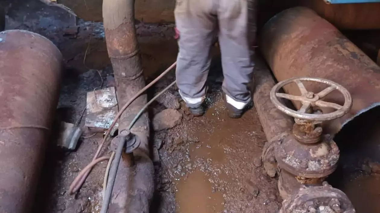 Un bărbat care stă cu spatele lucrează la sistemul de termoficare, unde se văd niște țevi de apă